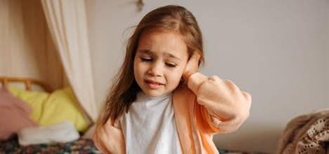 Copil care se ține de ureche, simțind durere, un posibil semn de otită.