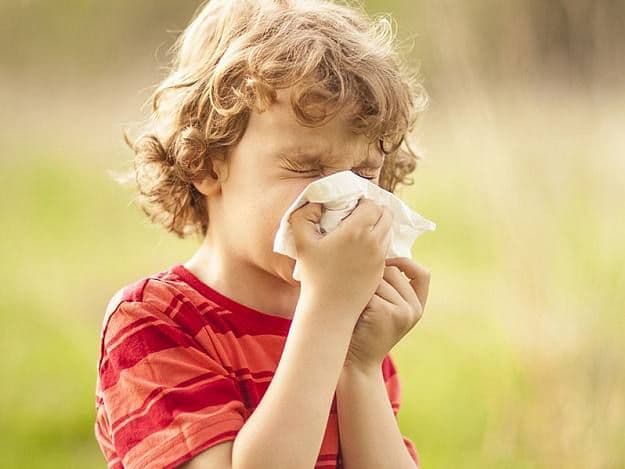 Copil care strănută în natură din cauza alergiilor sezoniere, primăvara