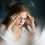Femeie cu ochii închiși care își ține capul, simțindu-se amețită.