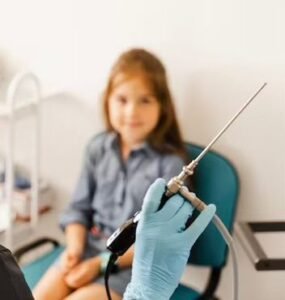 Fetiță zâmbitoare într-un cabinet medical, privind spre medicul care ține un videofibroscop.