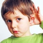 băiat care duce mâna la ureche, posibil semn de pierdere a auzului sau dificultăți auditive la copii