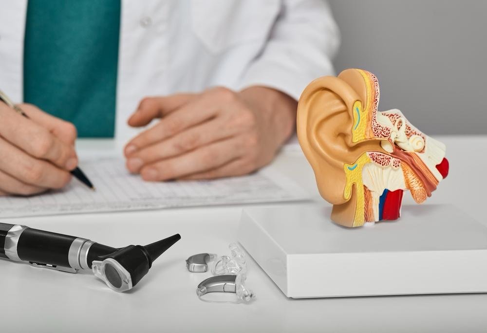 Model anatomic al urechii umane pe biroul unui medic ORL, alături de aparate auditive și un otoscop — simbol al prevenției și sănătății auditive la copii.