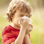 Copil care strănută în natură din cauza alergiilor sezoniere, primăvara