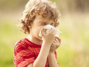 Copil care strănută în natură din cauza alergiilor sezoniere, primăvara