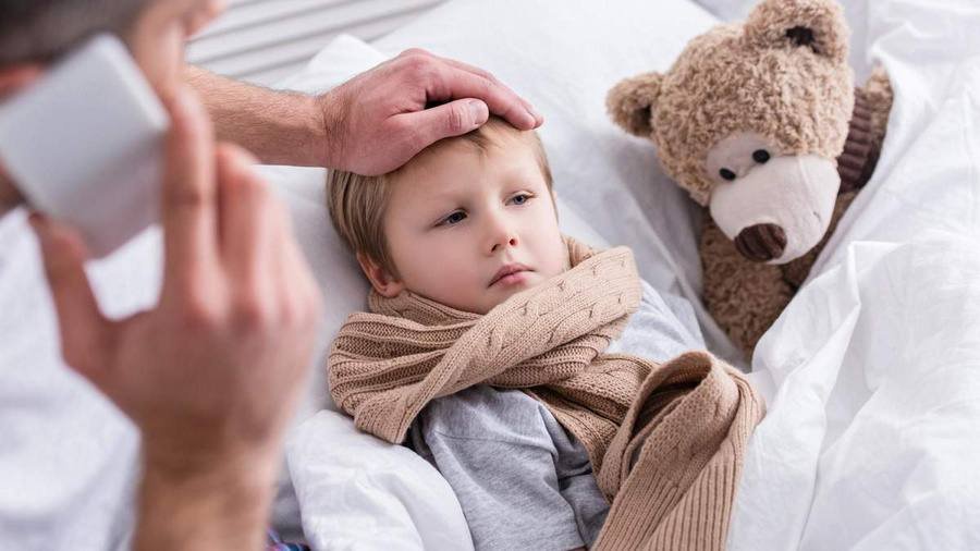 Mamă care aplică dezinfectant pe mâinile copilului, ambii purtând măști de protecție în timpul unei rutine zilnice de prevenție