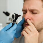 Examinare nazală realizată de medic ORL cu otoscop, pacient adult în cabinet medical, mâinile medicului în mănuși albastre