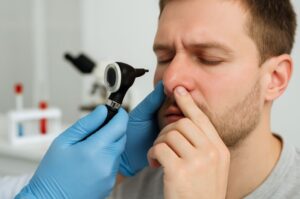 Examinare nazală realizată de medic ORL cu otoscop, pacient adult în cabinet medical, mâinile medicului în mănuși albastre