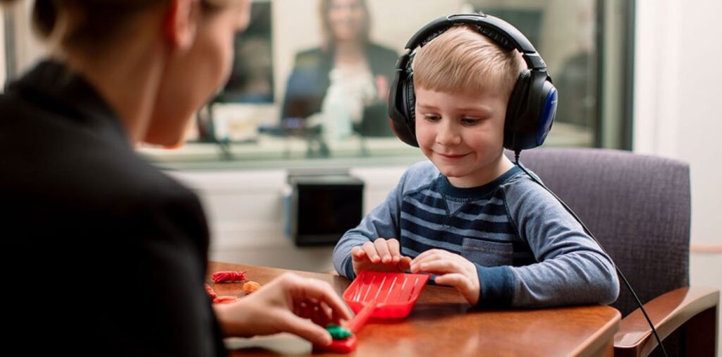 copil la test auditiv purtând căști, evaluare pentru implant cohlear în cabinet ORL